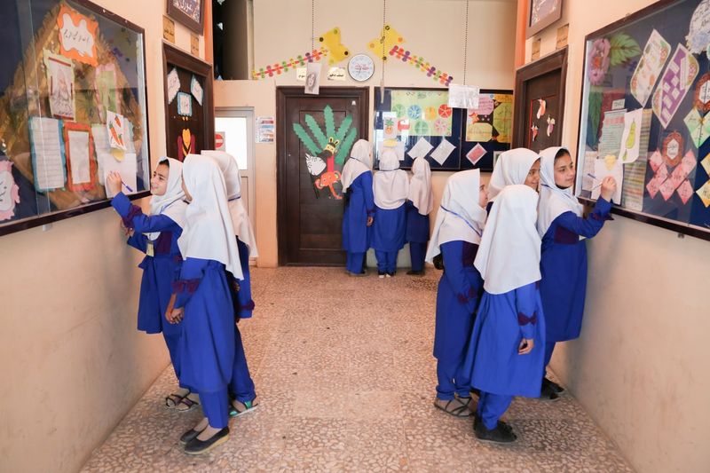 شاگردان با چادر سفید در دهلیز مکتب، در حال تماشای کارهای هنری