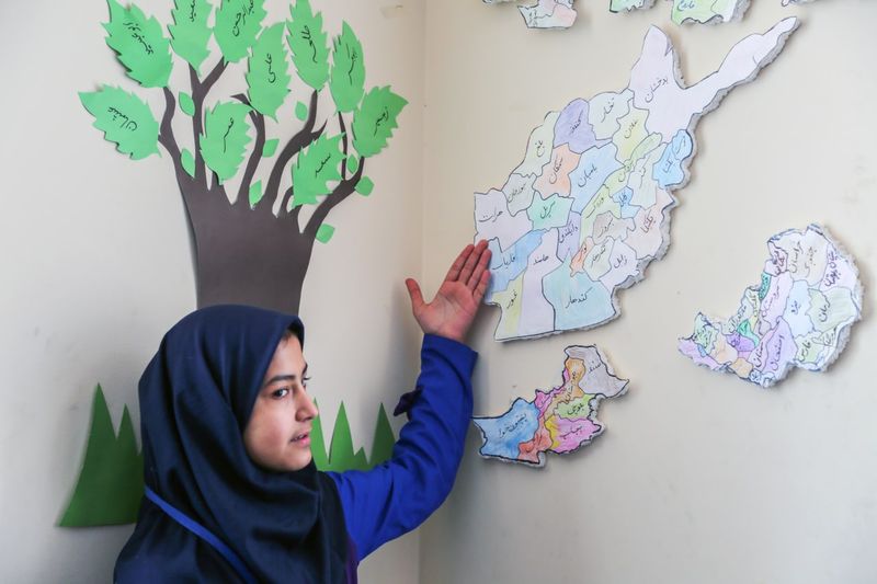 شاگردی با یونیفورم آبی در کنار نقشه افغانستان بر دیوار صنف